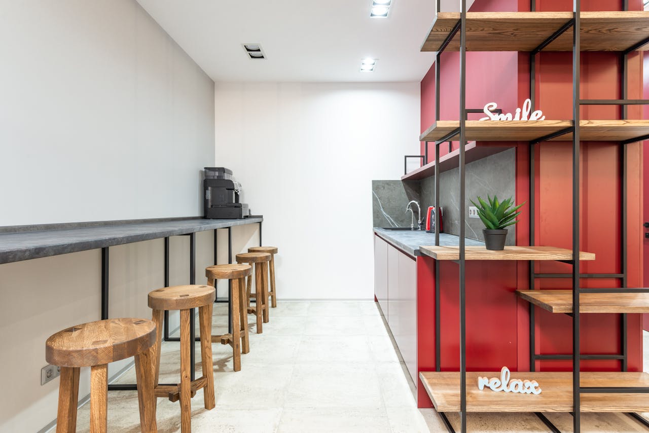 Interior of modern workplace with counter and stools next to open kitchen with cabinets near wooden shelves with potted plant and words relax and smile